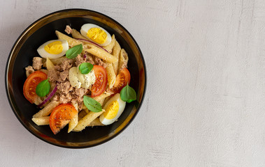 Tuna salad with pasta, tomatoes, and eggs in black bowl isolated on grey background. Healthy, vegetarian dinner or lunch. Italian homemade recipe. Close up, copy space.