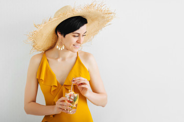 Young woman in yellow swimsuit and straw hat with a cocktail. Summer Vacation concept