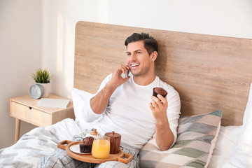 Fototapeta na wymiar Morning of handsome young man talking by mobile phone during breakfast in bed