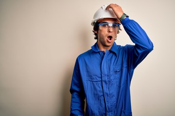 Young constructor man wearing uniform and security helmet over isolated white background surprised with hand on head for mistake, remember error. Forgot, bad memory concept.