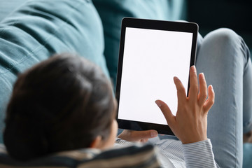 Close up Indian female typing on computer tablet screen blank white mockup, relaxing on cozy sofa at home, young female holding electronic device, surfing internet, reading book, chatting online