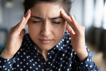 Close up exhausted Indian girl touching forehead, unhappy upset girl suffering from strong headache...