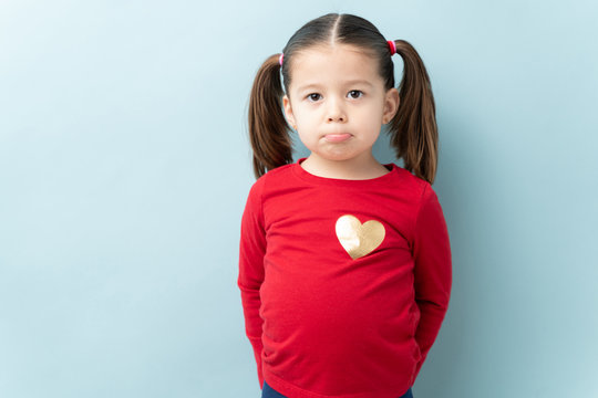 Portrait of a cute little girl with ponytails pouting and looking sad against a blue background in a studio