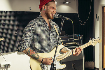 young caucasian guitarist contemporaneously play guitar and sing a song in recording studio....