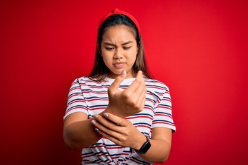 Young beautiful asian girl wearing casual striped t-shirt over isolated red background Suffering...
