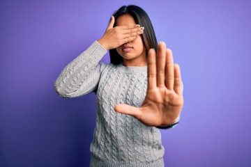 Young beautiful asian girl wearing casual sweater standing over isolated purple background covering eyes with hands and doing stop gesture with sad and fear expression. Embarrassed and negative