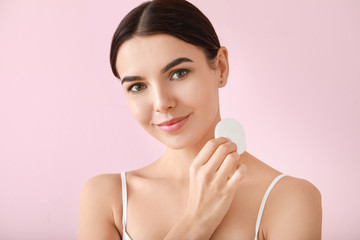 Beautiful young woman with cotton pad on color background © Pixel-Shot