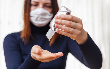 Woman in medical protective mask applying an antiseptic gel for hands disinfection and protection against flu virus. Coronavirus quarantine.