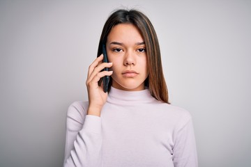 Beautiful brunette girl having conversation talking on the smartphone over white background with a confident expression on smart face thinking serious