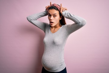 Young beautiful teenager girl pregnant expecting baby over isolated pink background doing funny...