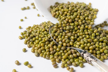 Heap of green mung beans in a white ceramic bowl on a white table close-up