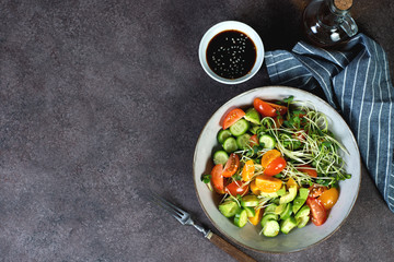 Vegan salad bowl with tomatoes, avocado, cucumber and microgreens on a dark background