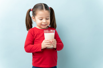 Pretty little girl enjoying a glass of milk and smiling in a studio