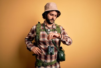 Young hiker man with curly hair and beard hiking wearing backpack and water canteen Checking the time on wrist watch, relaxed and confident
