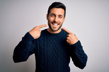 Young handsome man with beard wearing casual sweater standing over white background smiling cheerful showing and pointing with fingers teeth and mouth. Dental health concept.