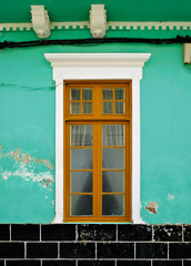 Obraz premium Old tall window with wooden frame in a green wall with flaking paint.
