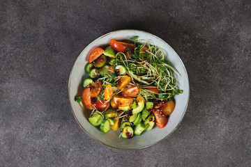 Vegan salad bowl with tomatoes, avocado, cucumber, micro greens and soy sauce on a dark background