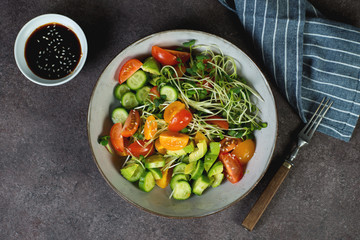 Vegan salad bowl with tomatoes, avocado, cucumber and microgreens on a dark background