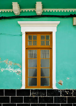 Old tall window with wooden frame in a green wall with flaking paint.