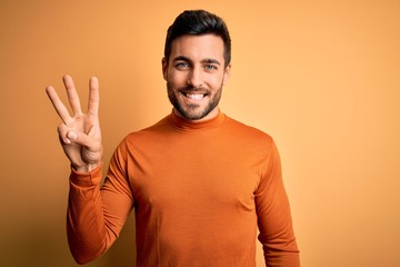 Young handsome man with beard wearing casual sweater standing over yellow background showing and...
