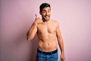 Young handsome strong man with beard shirtless standing over isolated pink background smiling doing phone gesture with hand and fingers like talking on the telephone. Communicating concepts.