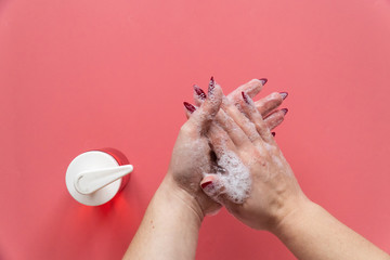 Woman soaps hands with liquid soap on pink background