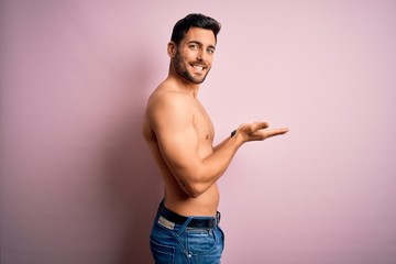 Young handsome strong man with beard shirtless standing over isolated pink background pointing aside with hands open palms showing copy space, presenting advertisement smiling excited happy