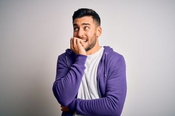Young handsome man wearing purple sweatshirt standing over isolated white background looking stressed and nervous with hands on mouth biting nails. Anxiety problem.