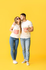 Happy young couple with popcorn watching movie on color background