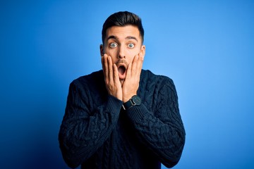 Young handsome man wearing casual sweater standing over isolated blue background afraid and...