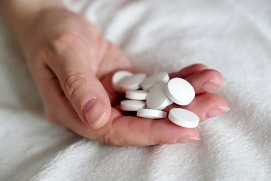White pills in a palm of female hand on the bed. Concept of medication, vitamins or sleeping pill