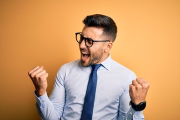 Young handsome businessman wearing tie and glasses standing over yellow background very happy and...