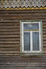 Fototapeta na wymiar Old wooden wall of a house with one window. Brown weathered horizontal planks. Paint peeling off from white window frame. Lace curtains behind glass. 
