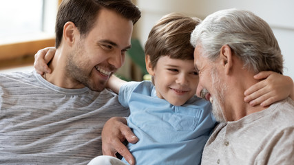 Overjoyed three generations of men hug cuddle enjoy weekend at home together, happy little...