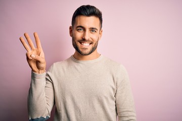 Naklejka premium Young handsome man wearing casual sweater standing over isolated pink background showing and pointing up with fingers number three while smiling confident and happy.