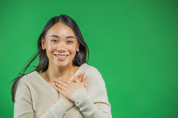 Fototapeta premium Happy young asian woman with hands on breast. Portrait of beautiful young female student holding hands near heart. The concept of education, women's struggle for life and justice