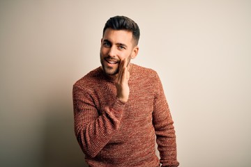Obraz premium Young handsome man wearing casual sweater standing over isolated white background hand on mouth telling secret rumor, whispering malicious talk conversation