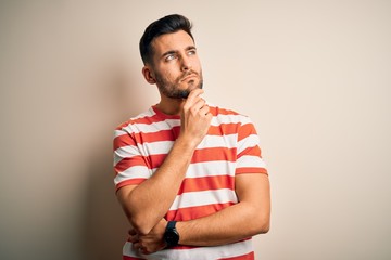 Young handsome man wearing casual striped t-shirt standing over isolated white background with hand on chin thinking about question, pensive expression. Smiling with thoughtful face. Doubt concept.