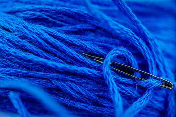 Macro close-up of needle threaded with blue thread. Bright blue colors, highly detailed texture.