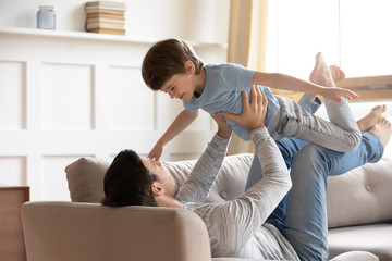 Happy young father relax in living room with small son playing together, overjoyed dad have fun...