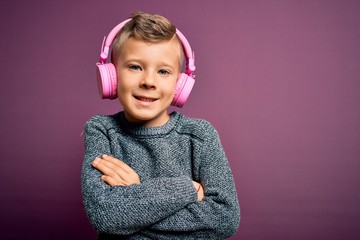 Young little caucasian kid wearing headphones listening to music over purple background happy face smiling with crossed arms looking at the camera. Positive person.