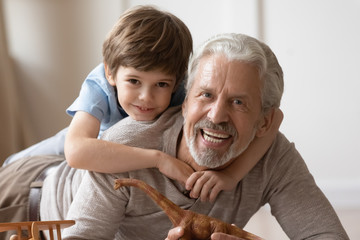 Portrait of happy little boy hug cuddle with overjoyed mature grandfather playing at home together, smiling small preschooler grandchild posing look at camera embracing smiling senior grandparent - obrazy, fototapety, plakaty