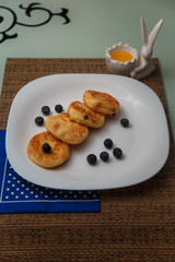 Syrniki or cottage cheese pancakes with blueberries and honey on white plate with blue napkin on kitchen table. Healthy breakfast, diet concept.