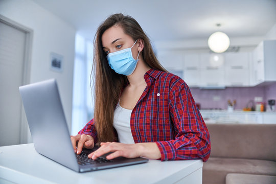 Young business woman in a medical protective mask works from home at the computer during self-isolation and quarantine. Virus coronavirus outbreak, flu epidemic and covid ncov novel