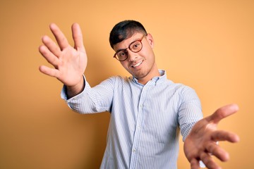 Young handsome hispanic business man wearing nerd glasses over yellow background looking at the...