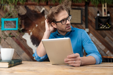 casual man holding his tablet while scratching head pensive