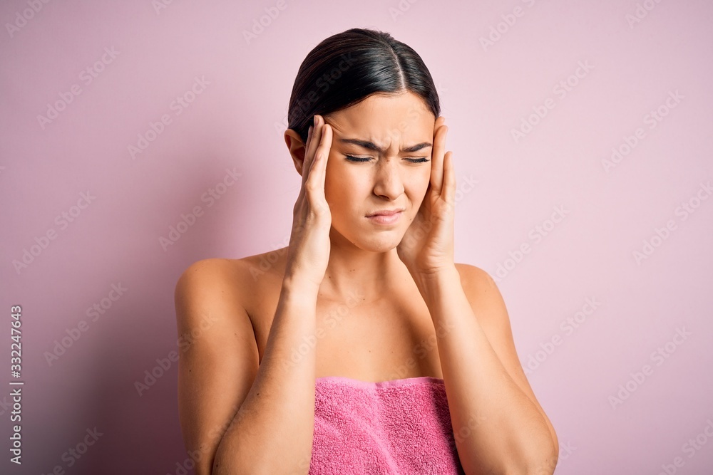 Poster Young beautiful girl wearing towel shower after bath standing over isolated pink background suffering from headache desperate and stressed because pain and migraine. Hands on head.