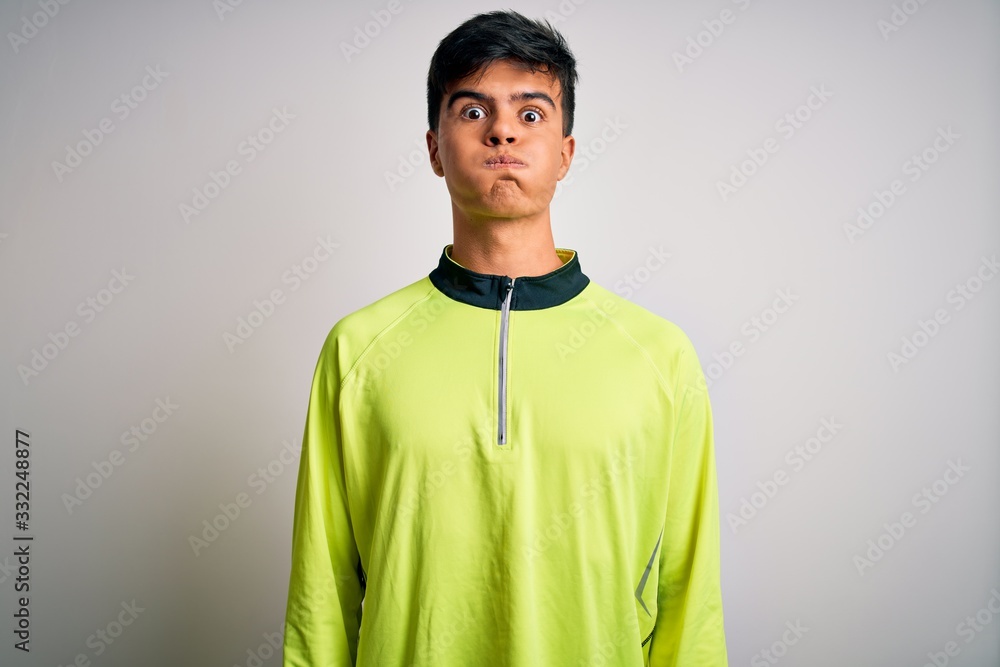 Canvas Prints Young handsome sportsman doing sport wearing sportswear over isolated white background puffing cheeks with funny face. Mouth inflated with air, crazy expression.