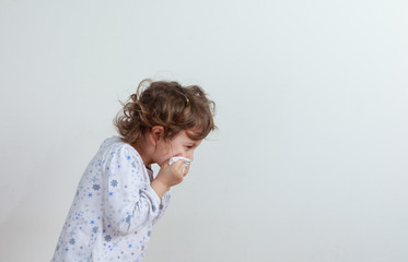 Young girl sneezing into a paper handkerchief, facing away, in front of a white background.