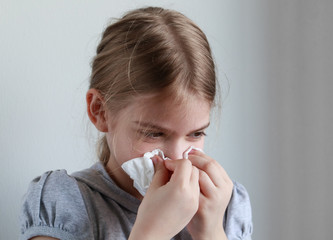 Young girl blowing her nose into a paper handkerchief in front of a white background.